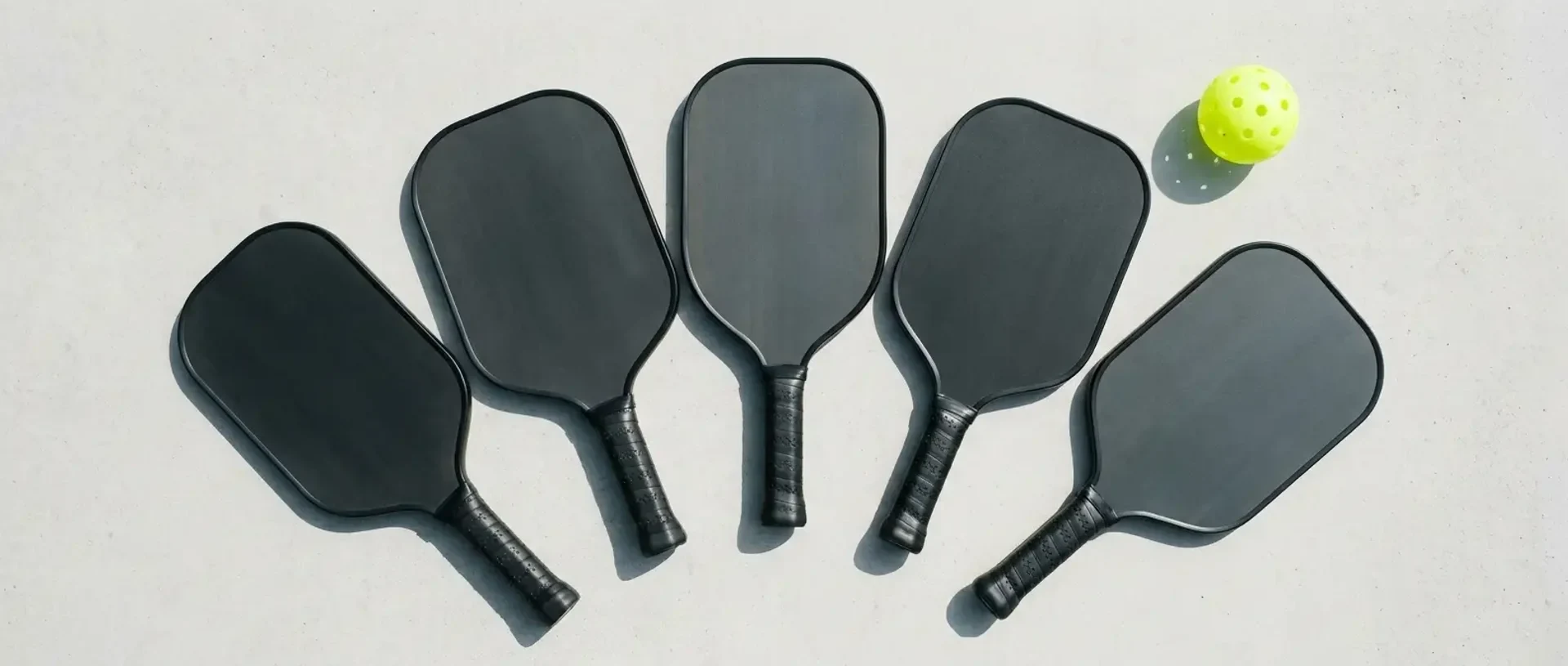A pickleball player tests the grip of a thermoformed paddle in a specialty shop with a rack of additional paddles soft in the background — illustrating how to choose a pickleball paddle.