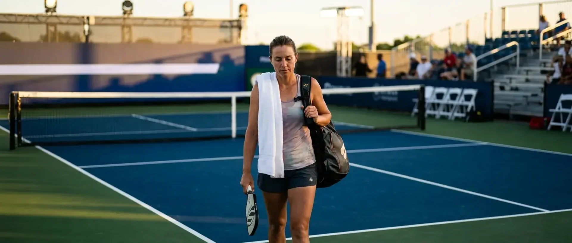 A pickleball pro walks off-court after a match with a towel over one shoulder and tournament backdrop soft behind — illustrating how to go pro in pickleball.