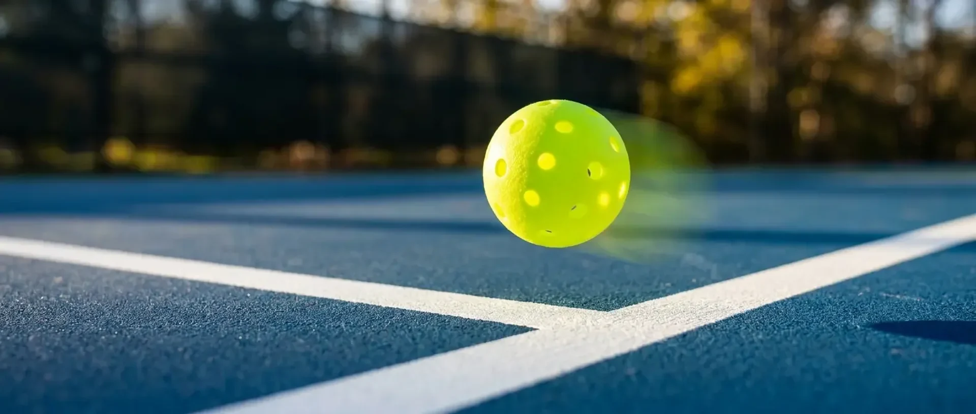 An open rulebook rests on a courtside bench beside a paddle, ball, and water bottle — illustrating the 2026 pickleball rules summary.