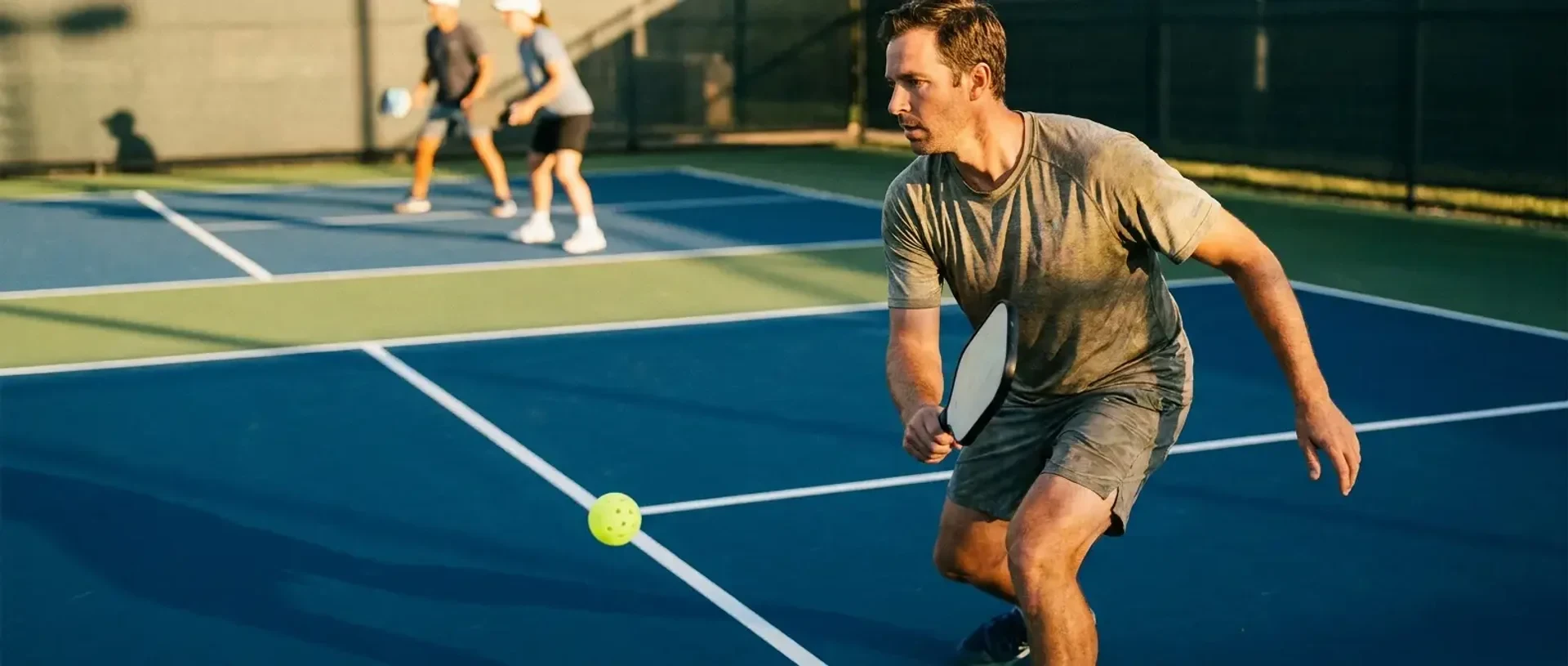 Two adjacent pickleball courts in open play — a beginner rally on one and an advanced kitchen-line rally on the other — illustrating skill-level differences from 2.0 to 5.0+.